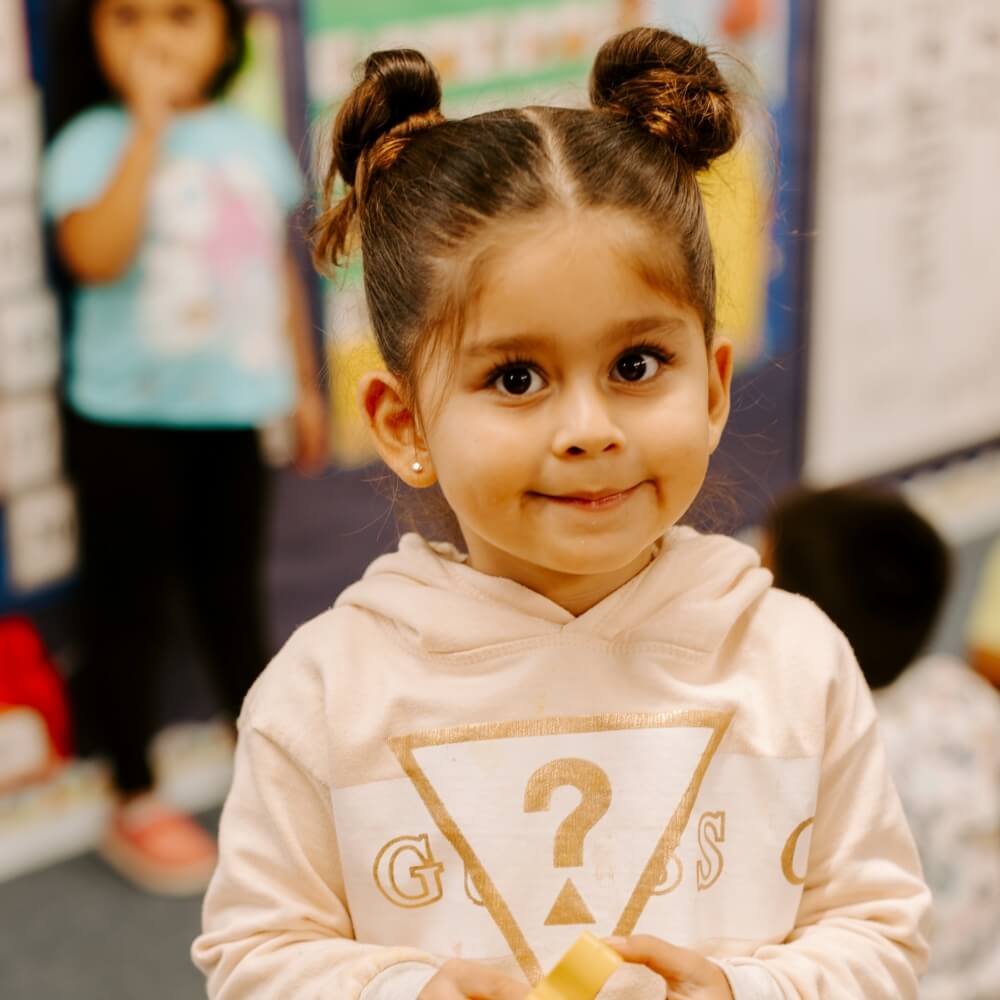 A young girl in a classroom holding a puzzle piece, representing curiosity and early learning.