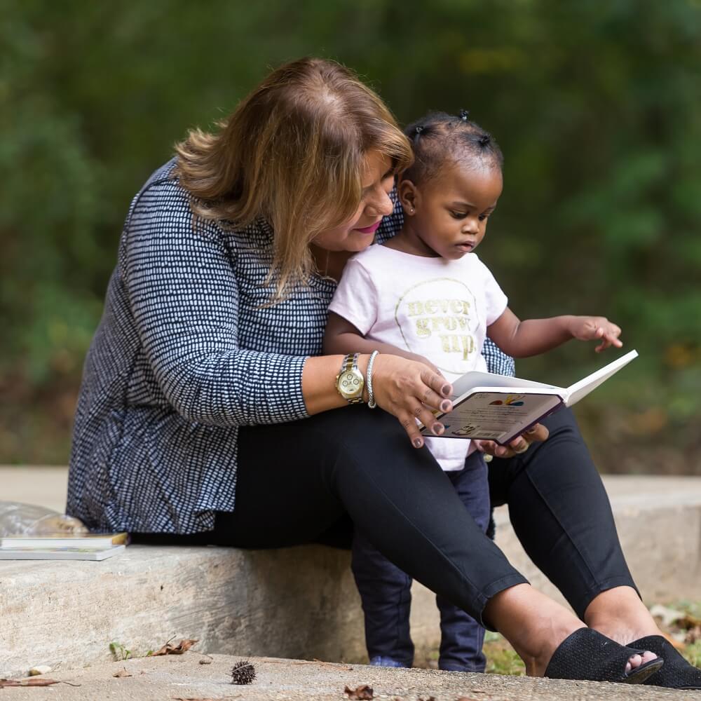 An Excel By Eight member reading a book to a young child outdoors, emphasizing the importance of early literacy.
