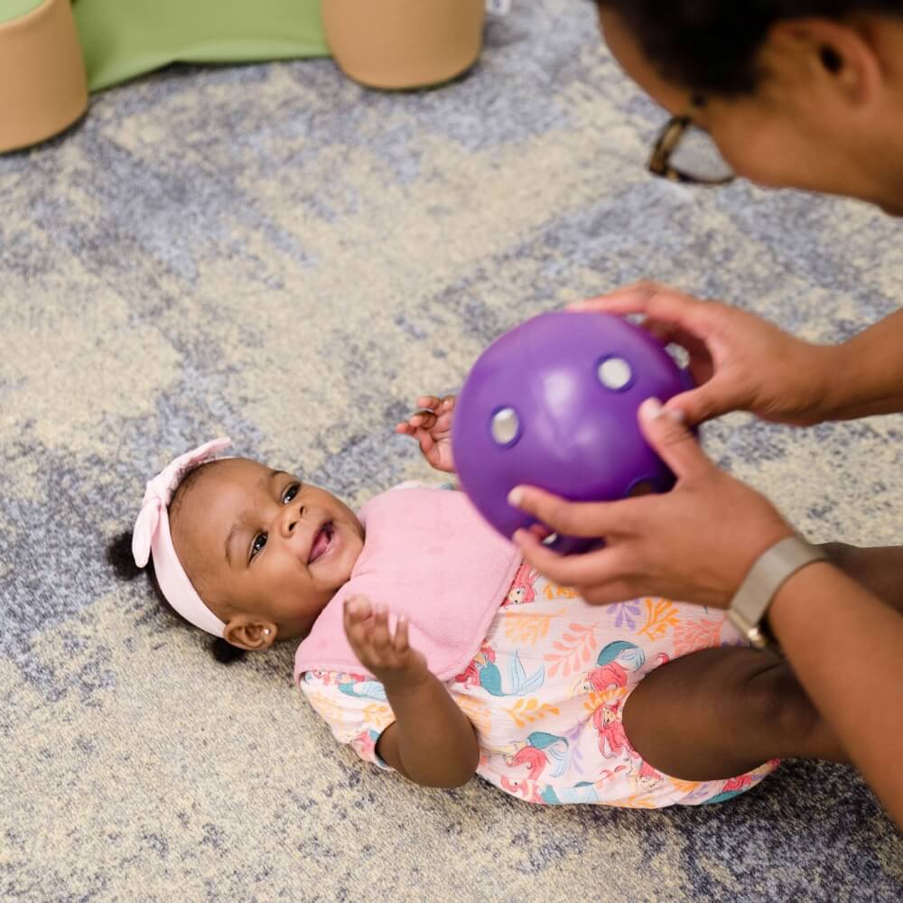Teacher playing with a baby, emphasizing nurturing relationships.
